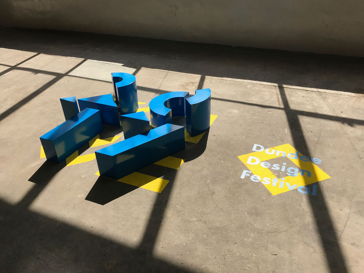 3 dimensional blocks representing the Dundee Design Festival 2017 logo lie on a concrete floor.