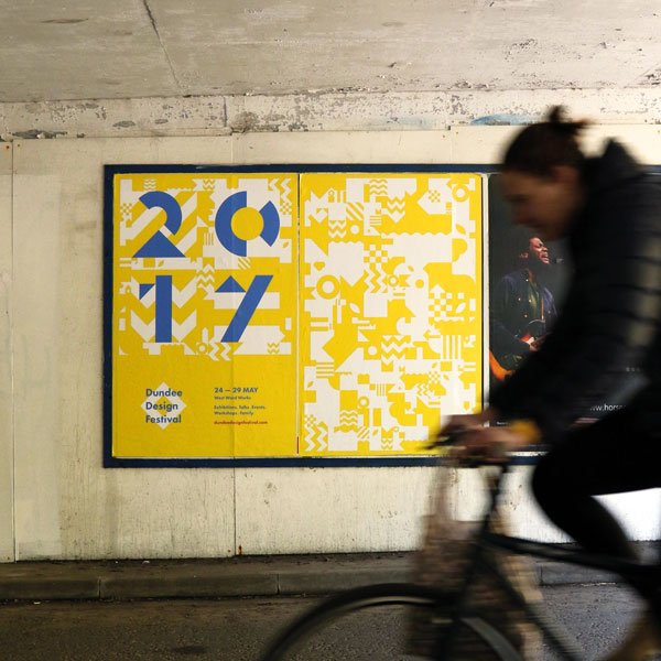 Blurred figure on a bike passes festival posters.