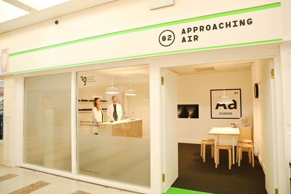 Approaching Air sign above the door of a minimallist shop space. A man and a woman stand inside in lab coats.
