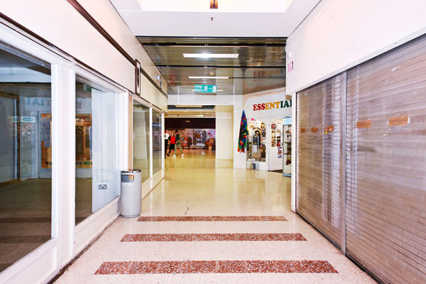 Interior corridor of shopping centre with empty windows and shutters down.