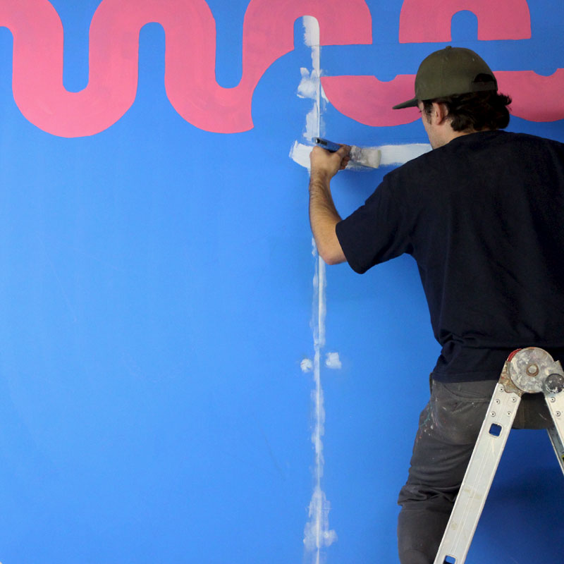 Man on a ladder carefully paints a shape.