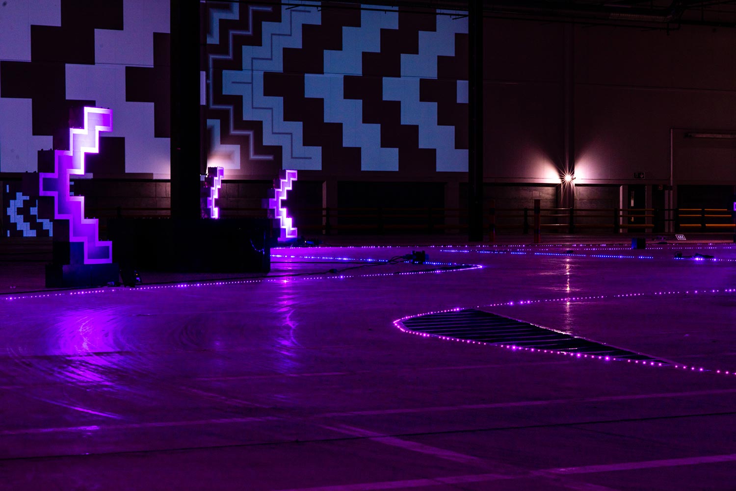 Purple illuminated warehouse space with giant glowing arrows.