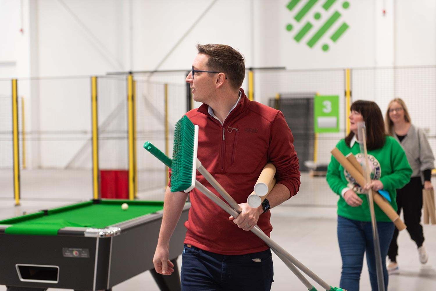 3 people look to their left while carrying brooms and poles.