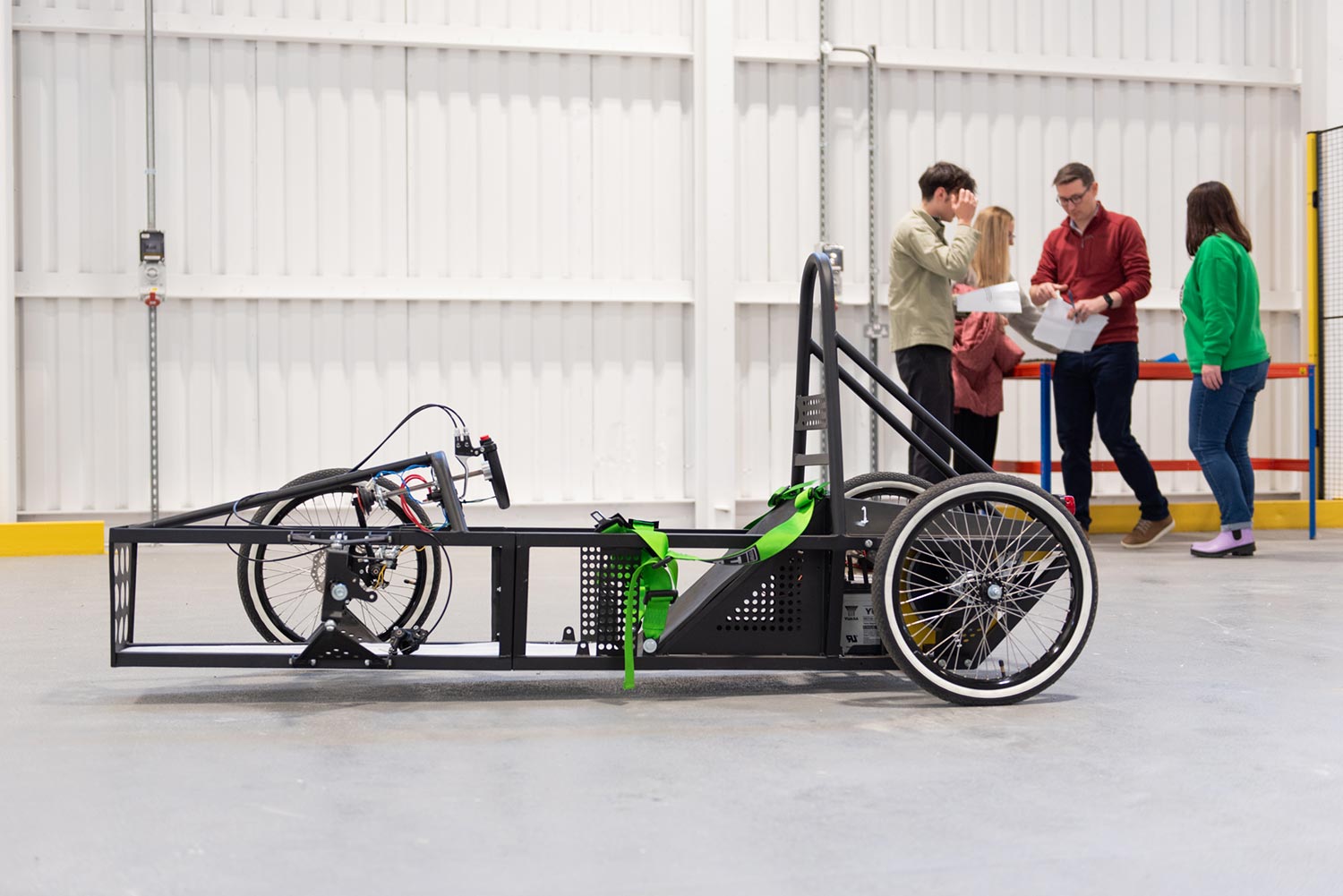 Man on a static bike indoors pedals as people look on.