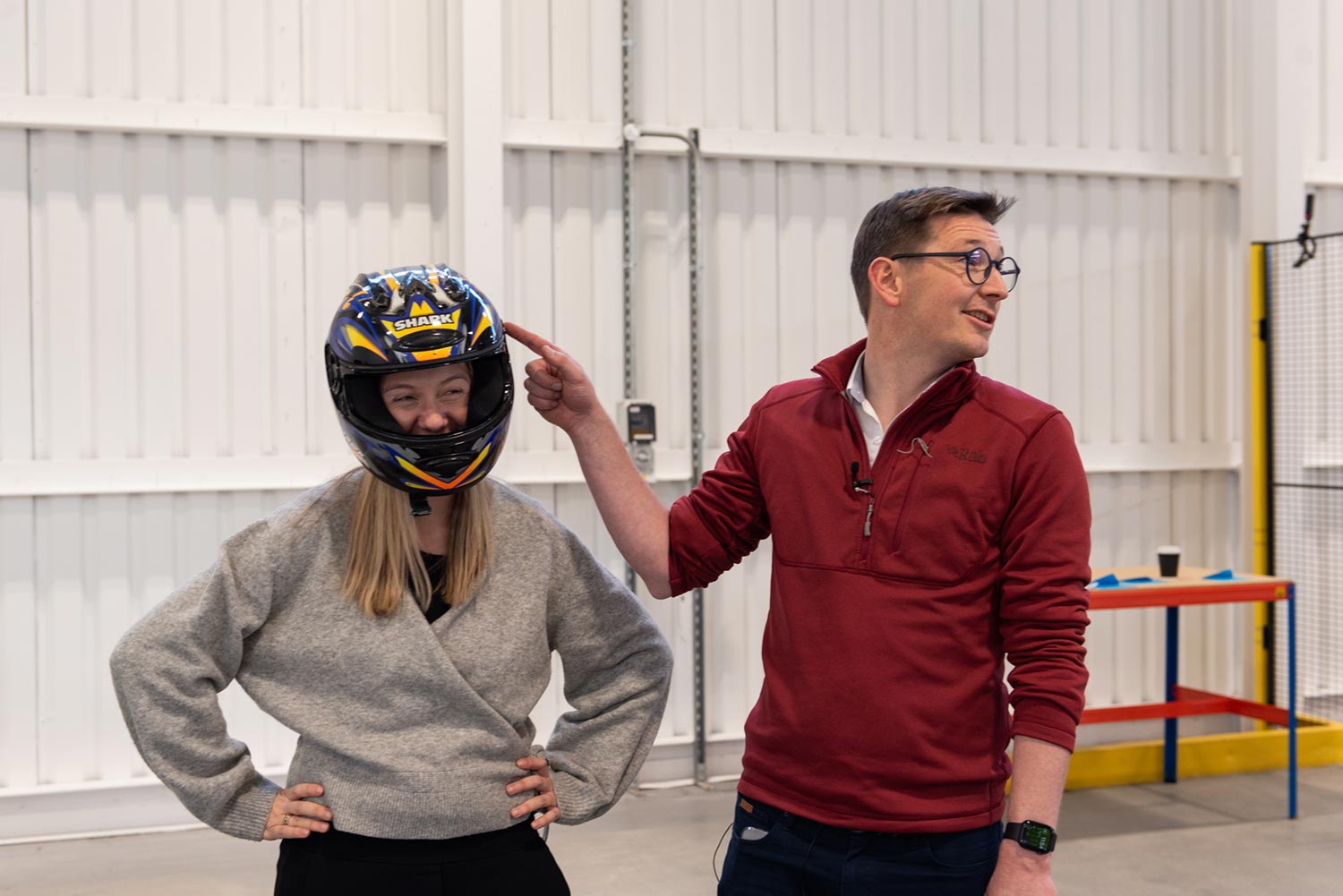 Woman laughing while wearing crash helmet and man beside her points to her head.