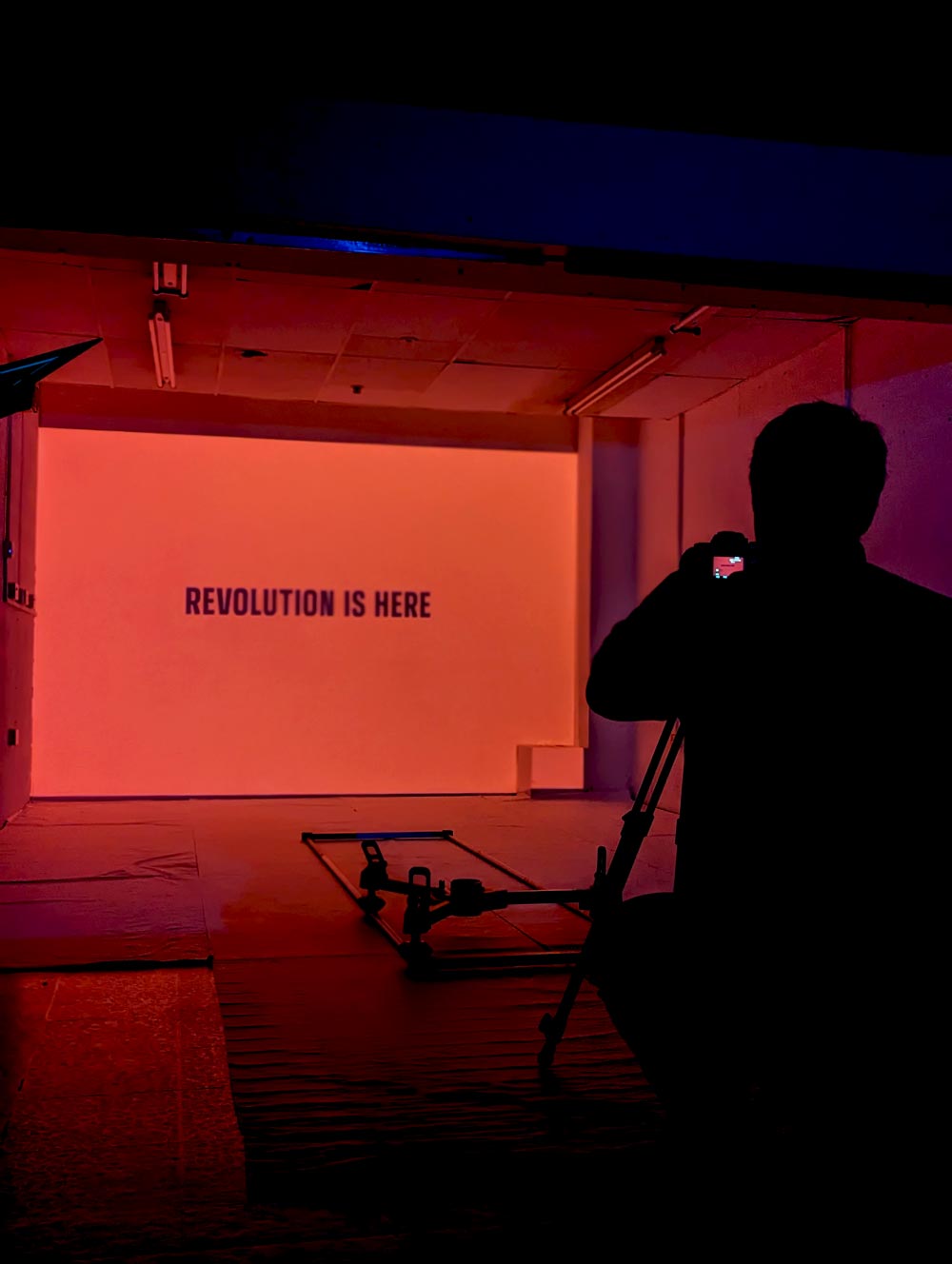 Man behind a tripod adjusts camera pointing into a red room.