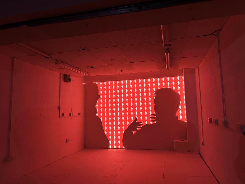 The silhouettes of mutiple people are cast into a room full of red and white graphics.