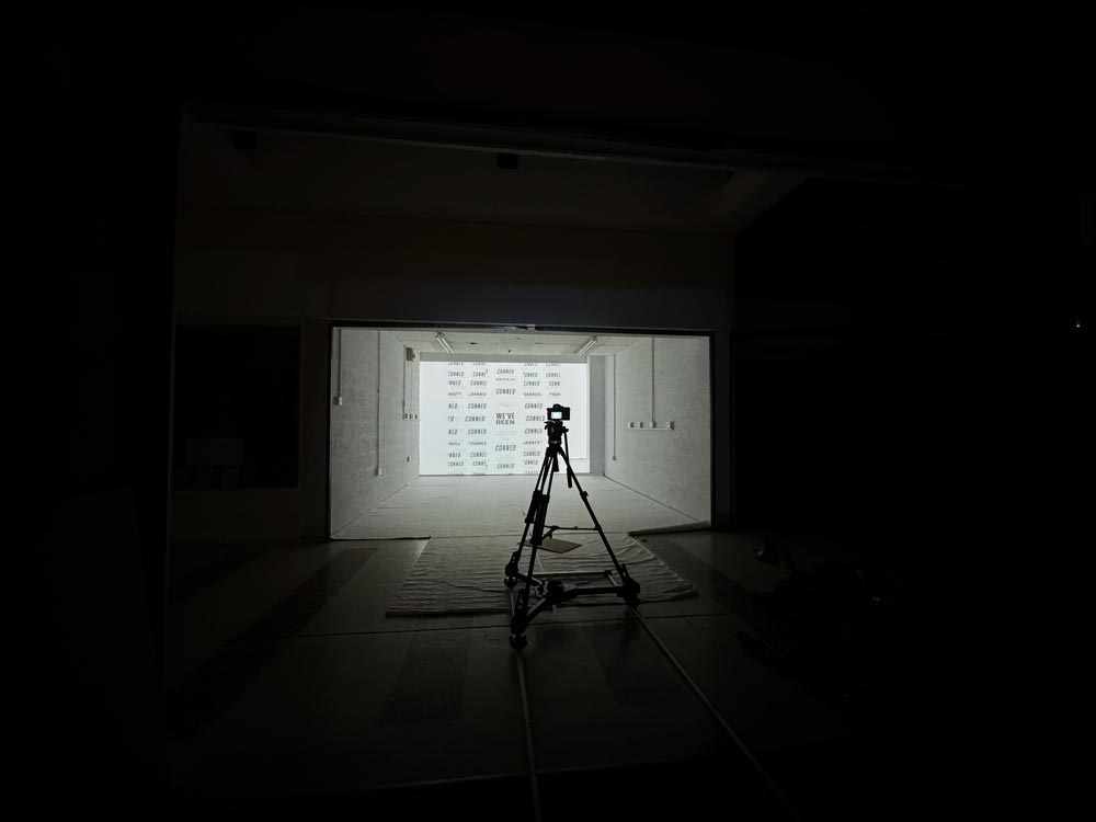 A tripod is silhouetted with a white room lit up in the distance.
