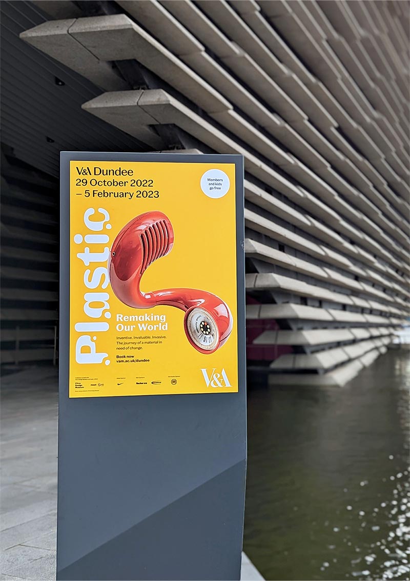 Yellow poster for V&A Dundee Plastic exhibition on poster stand outside the museum.